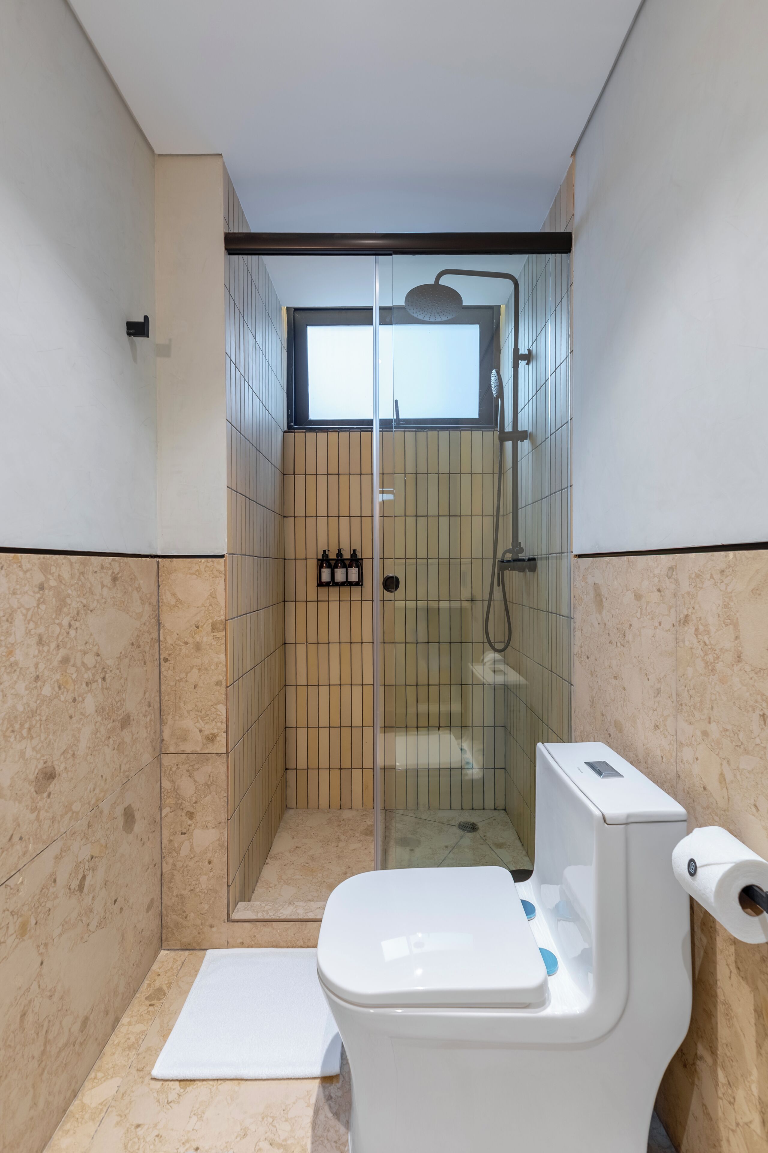 A bathroom with a glass-enclosed shower, a toilet, and a small shelf with bottles.