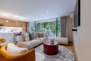 Una sala de estar moderna con sofá, sillones, una mesa de centro y una cocina con mesa y sillas.
