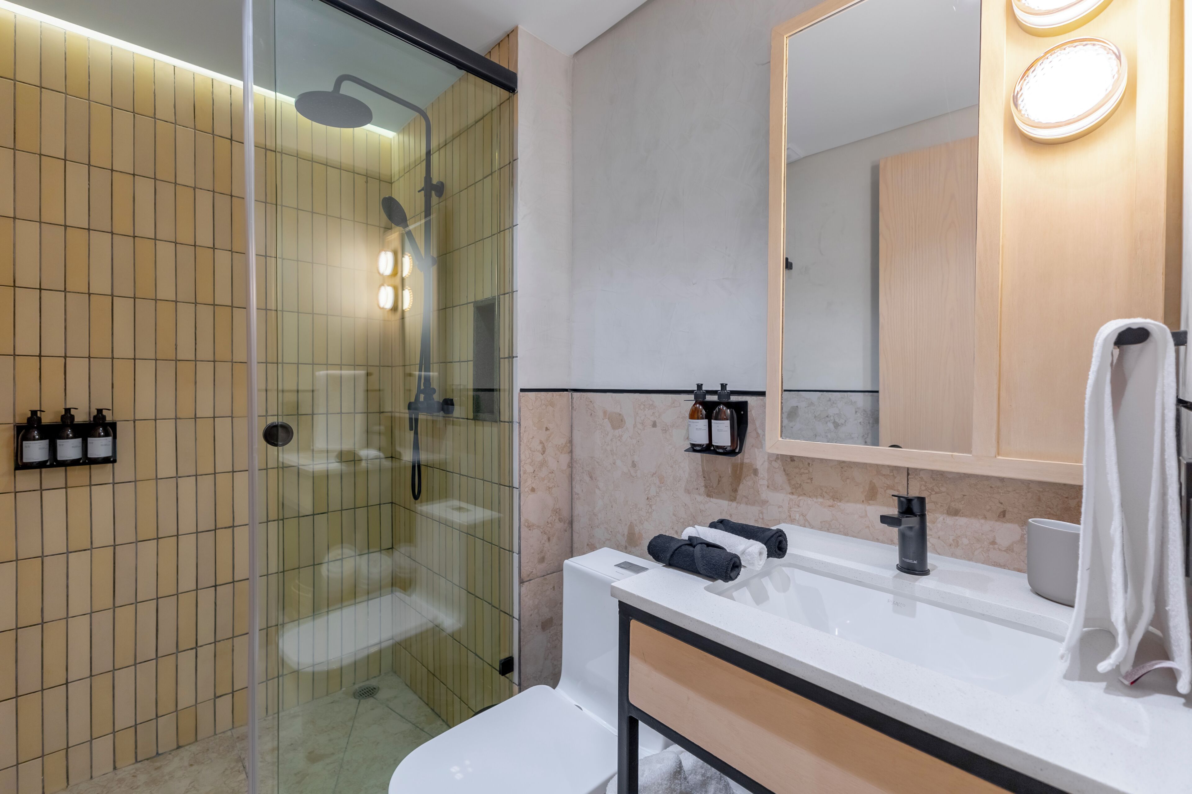 Un baño moderno con ducha de vidrio, un lavamanos blanco y un espejo grande.