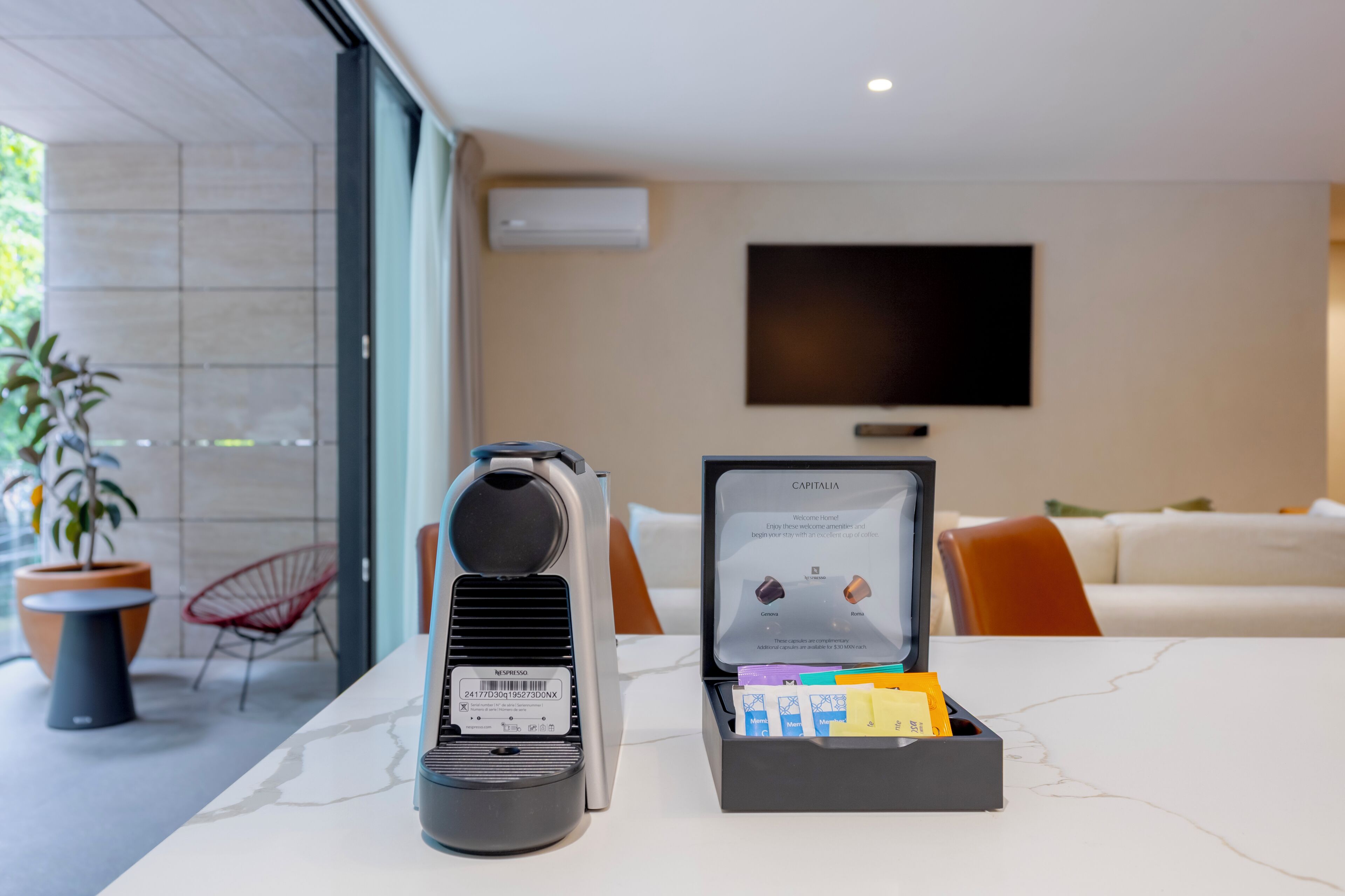 Una sala de estar moderna con una cafetera, una caja de cápsulas Nespresso y un televisor de pantalla plana en la pared.