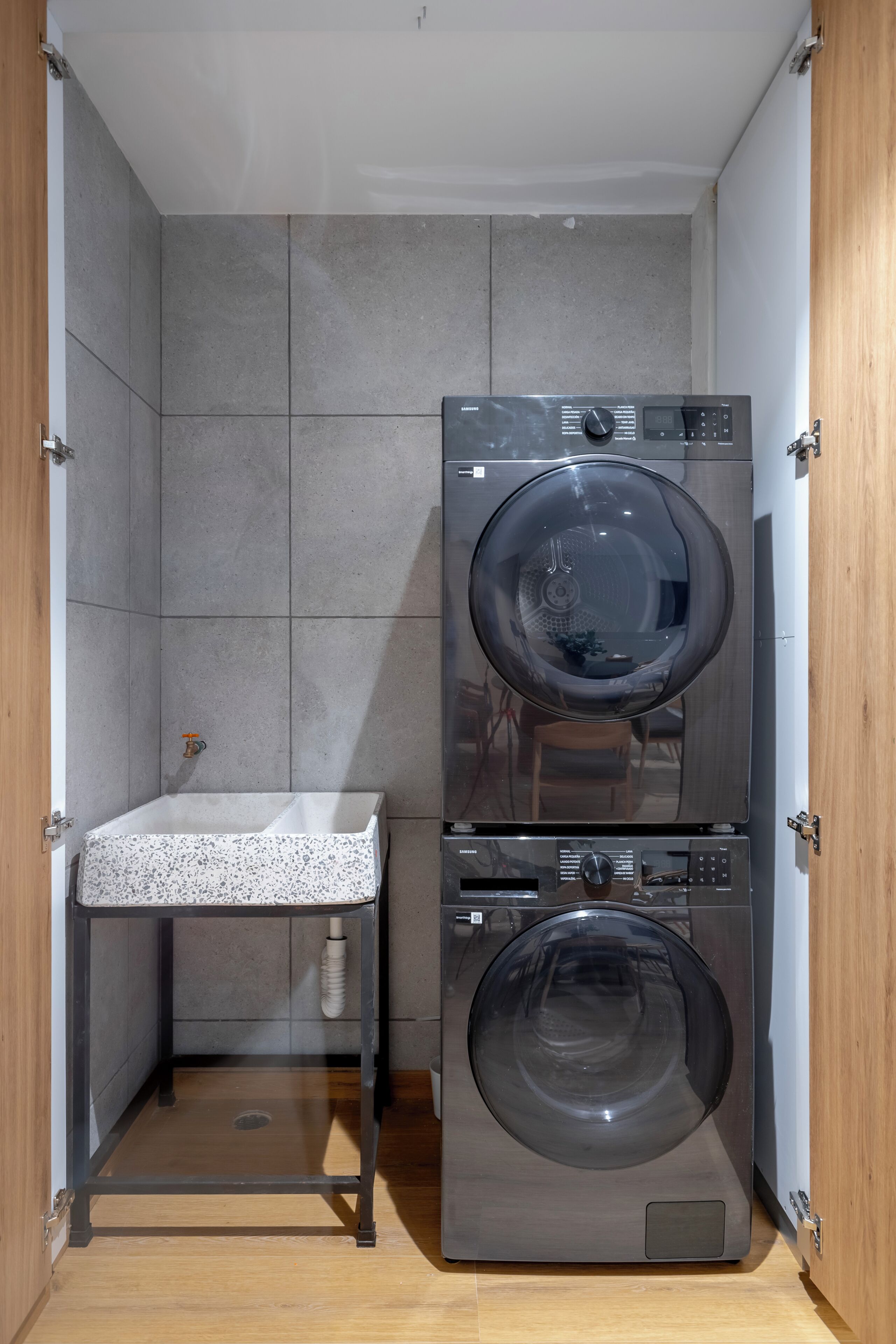 A compact laundry room with a washing machine and dryer stacked vertically, a small sink, and a towel rack.