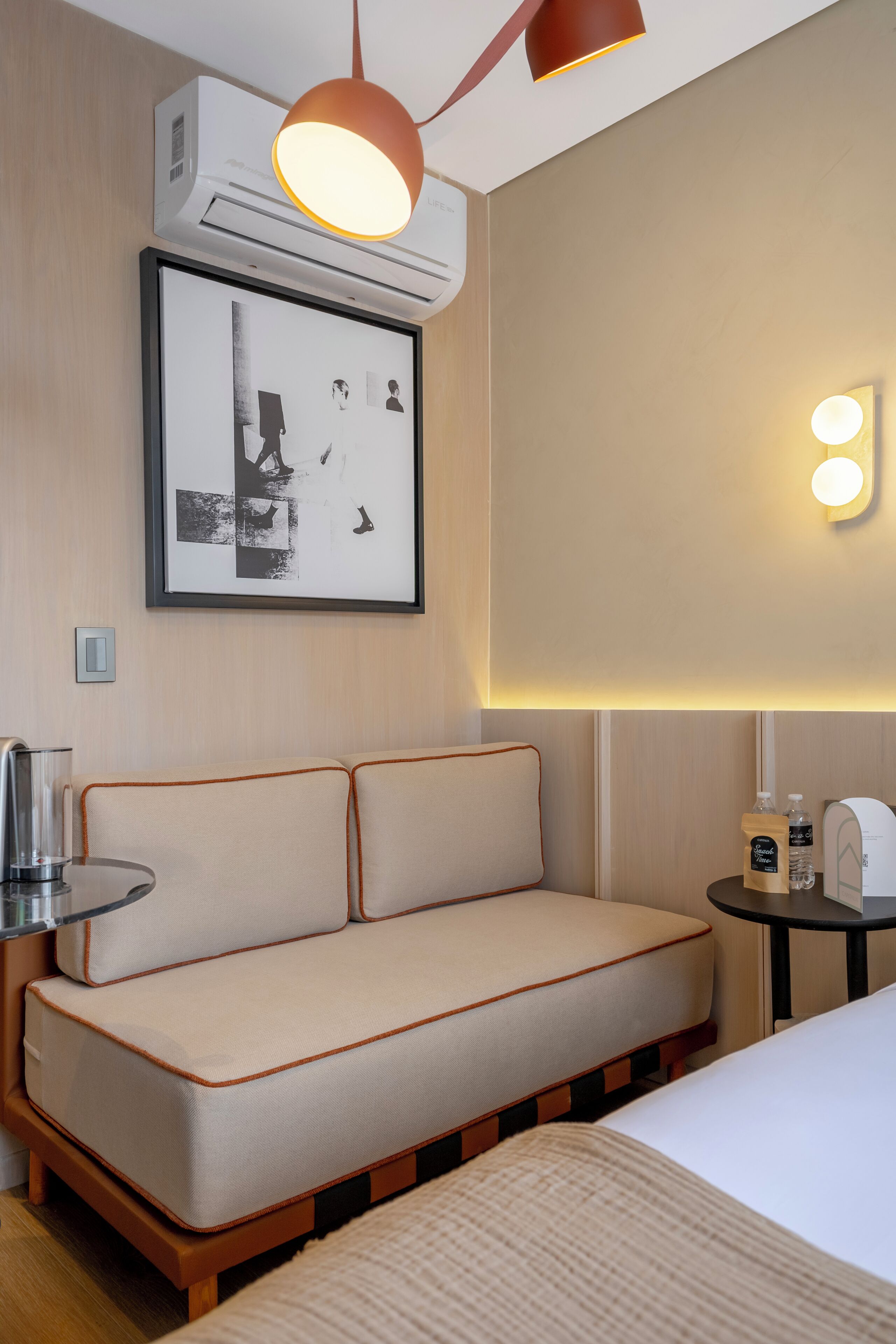 Habitación de hotel con sofá, mesita de noche con lámpara, cuadro en la pared y equipo de aire acondicionado.