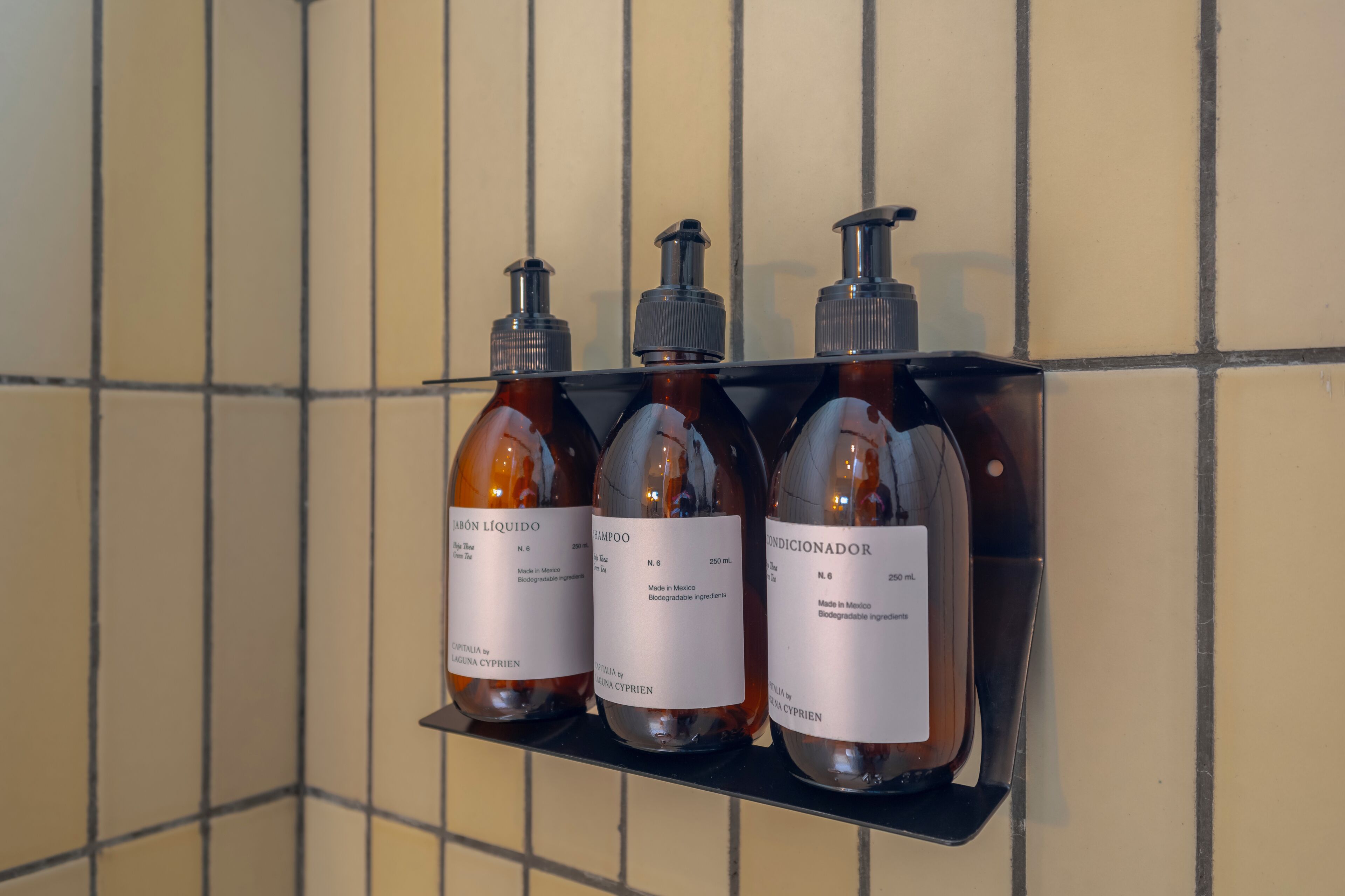 Tres botellas de champú y acondicionador sobre un estante negro frente a una pared de azulejos.