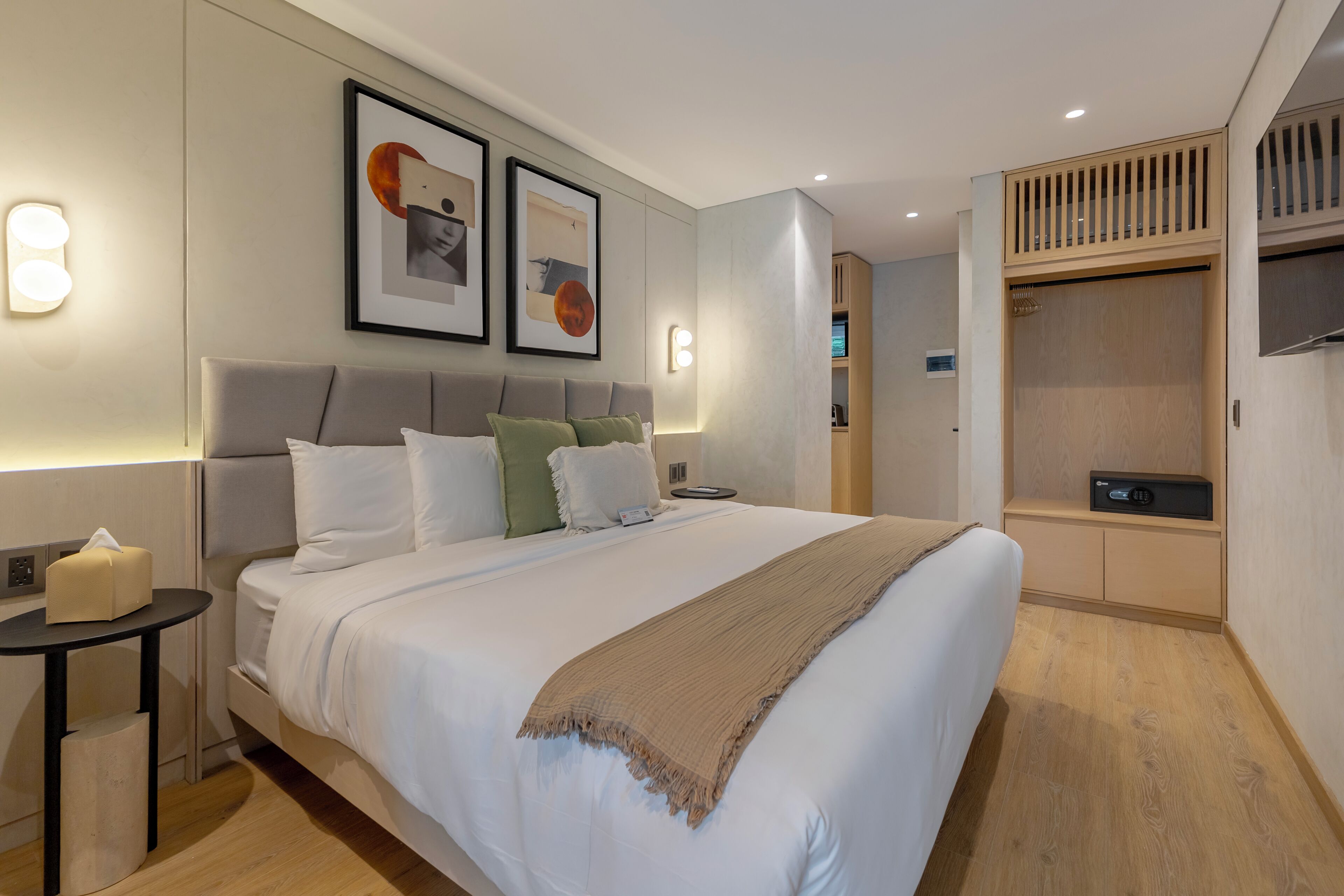A modern hotel room with a large bed, bedside tables, a wardrobe, and wall-mounted artwork.