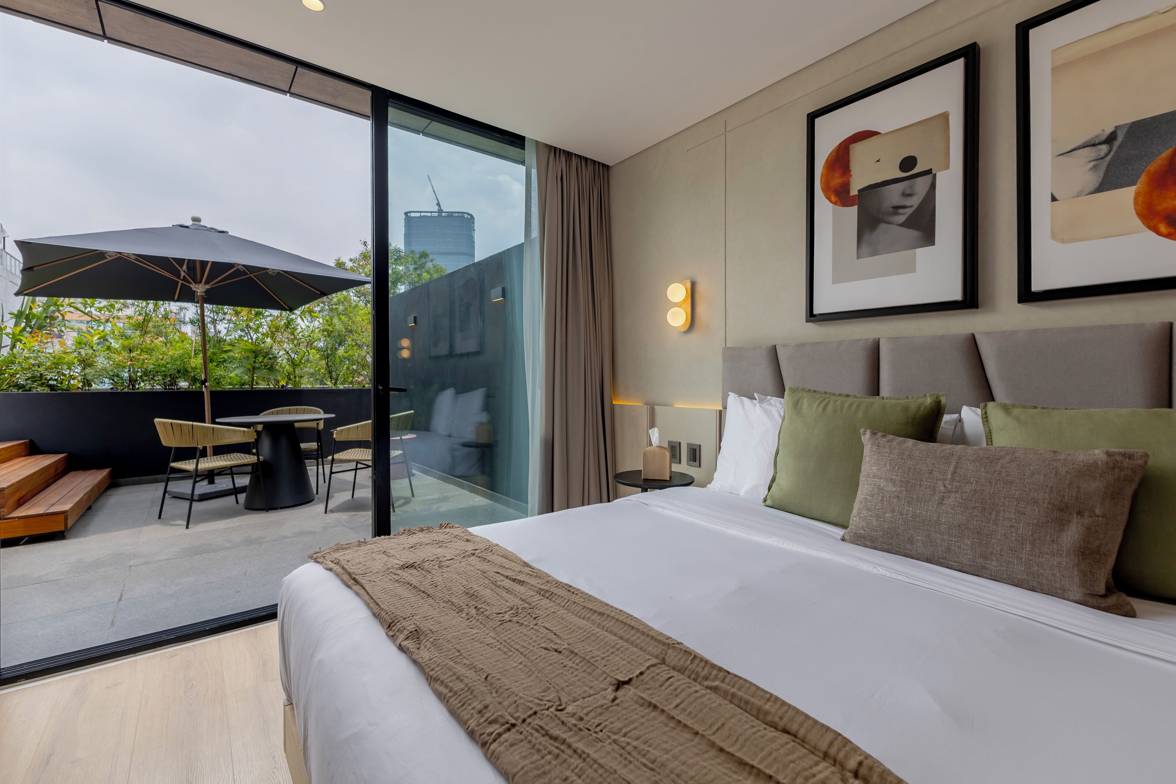 A modern hotel room with a large bed, a balcony with a table and chairs, and a city view.