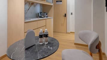 Een moderne eethoek met een ronde tafel, twee stoelen, een tafel met een marmeren blad, een zwarte vloerlamp en een houten wandplank met een marmeren achterwand.