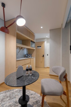 A modern dining area with a round table, two chairs, a marble-top table, a black floor lamp, and a wooden shelving unit with a marble backsplash.