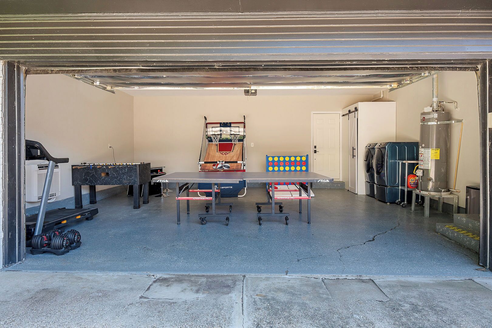 Een garage met een tafelvoetbaltafel, een pingpongtafel en een basketbalring.