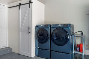 A laundry area with two front-loading washing machines, a white sliding door, and a small shelf with cleaning supplies. - Cozy 3BR - Near Dallas Zoo - Gym & Ping Pong (Dallas)