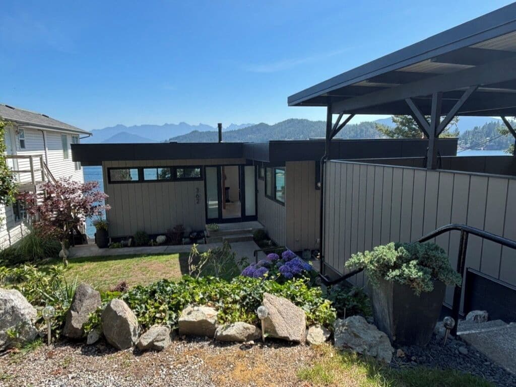 A modern house with a covered patio, a garden with rocks and plants, and a view of mountains.