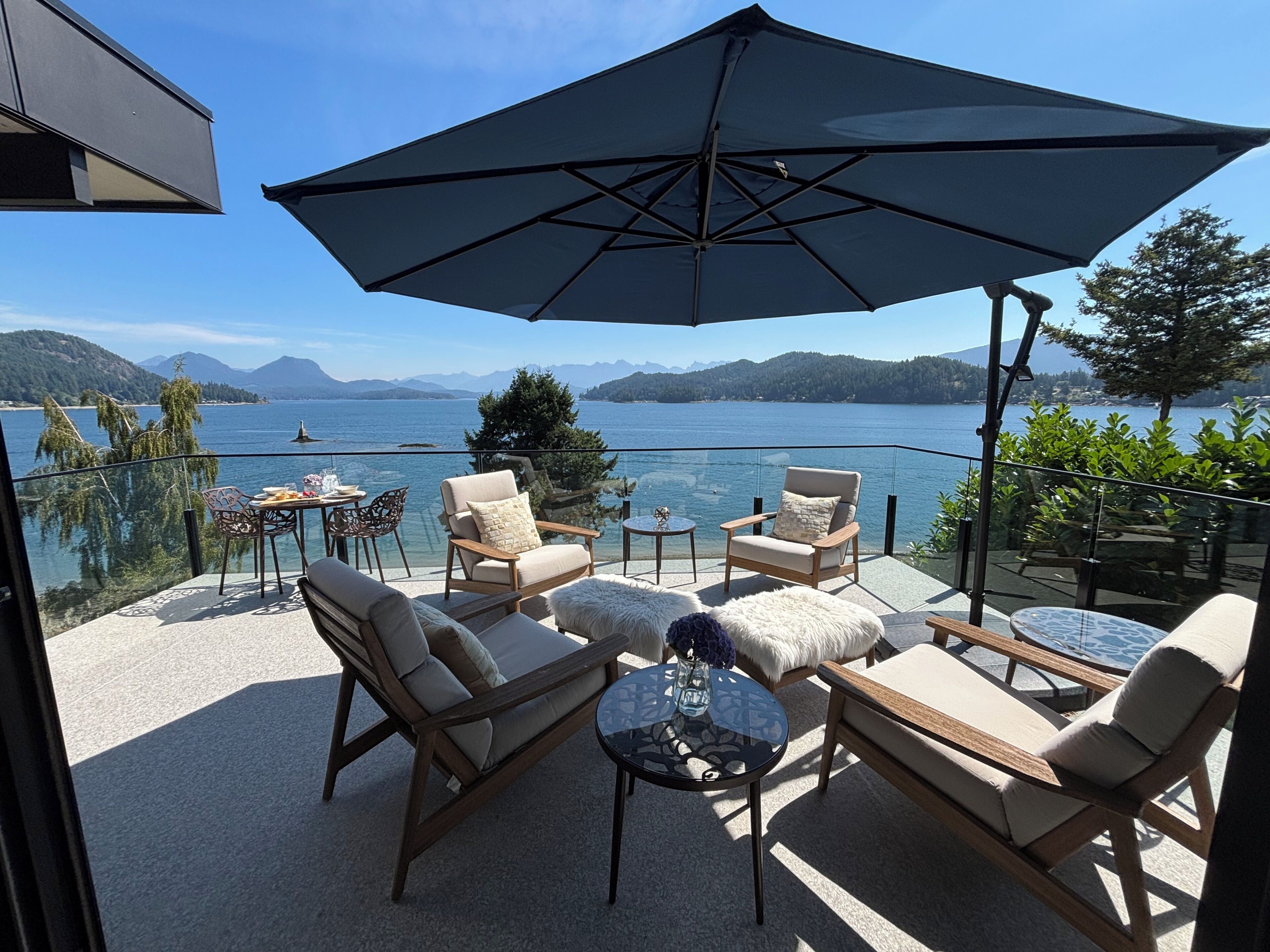 Eine Terrasse mit Sitzgelegenheit im Freien, einem großen Sonnenschirm und Blick auf einen See und Berge.