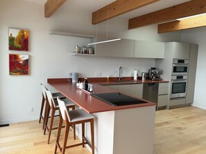 Cozinha moderna com ilha central, banquetas, forno embutido e máquina de café.