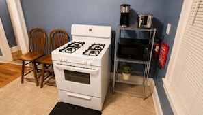 A kitchen with a white stove, two wooden chairs, a metal shelf with a plant, and a fire extinguisher. - Spacious 4-bedroom apartment in fabulous Dearborn with AC (Dearborn)