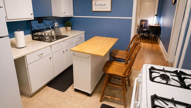 A compact kitchen with white cabinets, a wooden countertop, a stove, and a dining area with chairs. - Spacious 4-bedroom apartment in fabulous Dearborn with AC (Dearborn)