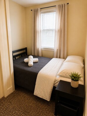A small, neatly arranged bedroom with a bed, a bedside table with a plant, and a window with curtains. - Spacious 4-bedroom apartment in fabulous Dearborn with AC (Dearborn)