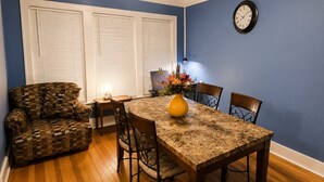 A dining area with a table, chairs, a vase with flowers, a clock on the wall, and a patterned sofa. - Spacious 4-bedroom apartment in fabulous Dearborn with AC (Dearborn)