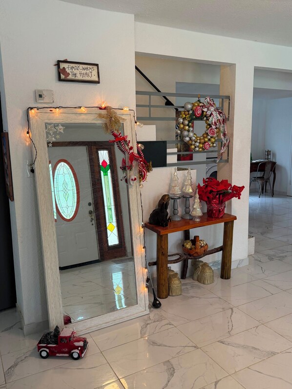 Un hall d’entrée décoré avec un miroir, une guirlande, une plante en pot et une petite table ornée d’objets décoratifs.
