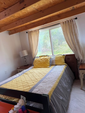 Ein Schlafzimmer mit Bett, Nachttisch, Lampe und einem Fenster mit Vorhängen.