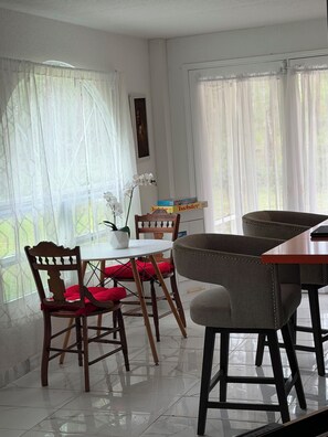 Un coin repas avec une table et des chaises, une plante en pot et une fenêtre ornée de rideaux légers.