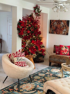 Ein Wohnzimmer mit Weihnachtsbaum, einem leopardenmuster-Pouff und einem Sessel mit Kissen, auf dem 'Believe' steht.