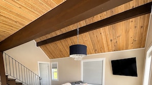 Una sala de estar moderna con un sofá seccional, piso de madera, una araña y un televisor montado en la pared.