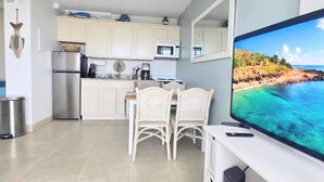 Una cocina moderna con armarios blancos, un refrigerador de acero inoxidable, un microondas y un comedor con sillas de mimbre.