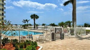 Área da piscina com deck cercado, espreguiçadeiras e vista para o mar.