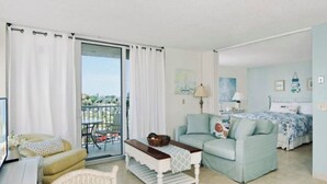 Una sala de estar con sofá, mesa de centro, silla de mimbre y balcón con vistas.