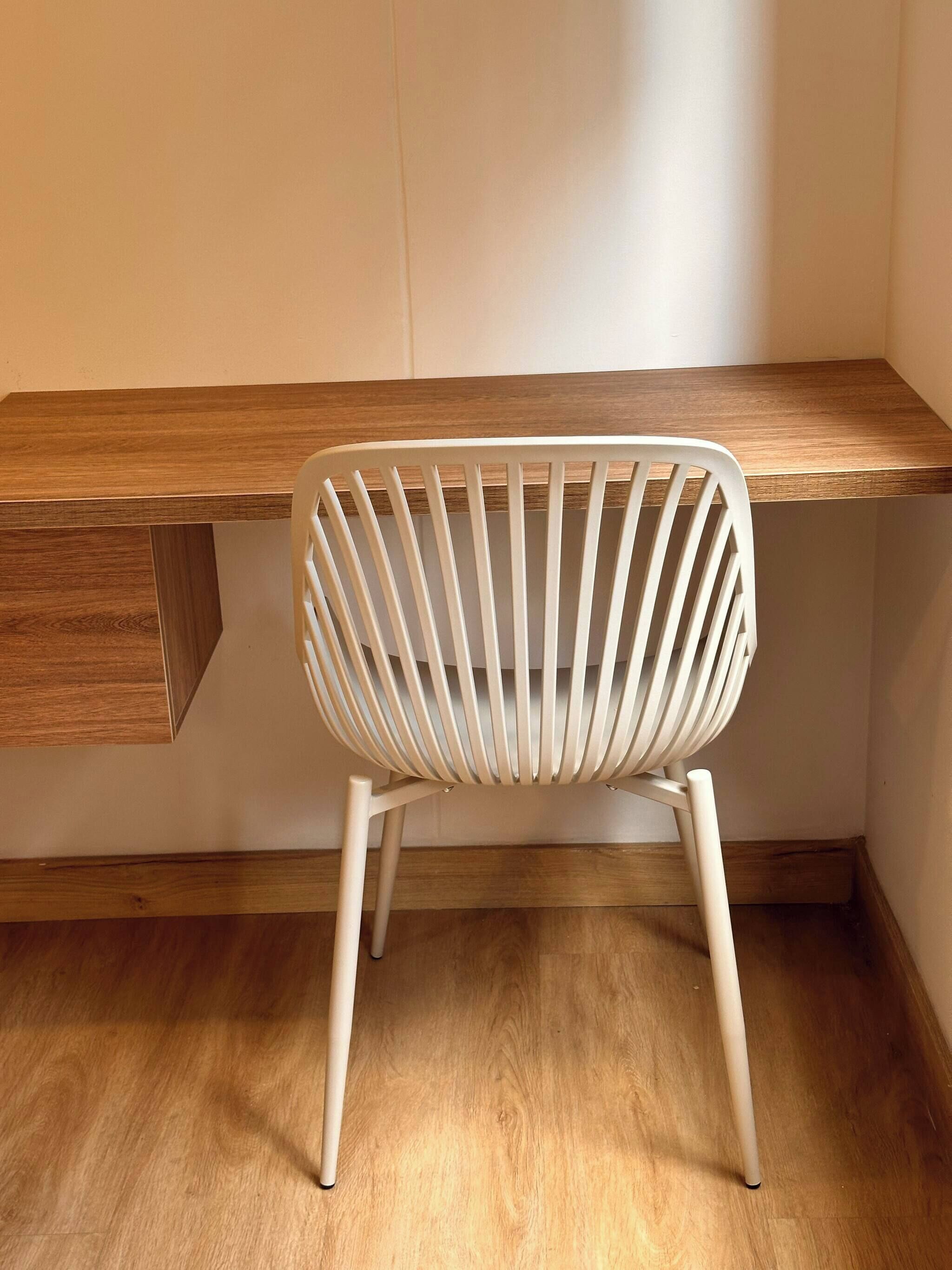 Une chaise blanche dont le dossier est constitué de lattes, placée devant un bureau en bois muni d’un tiroir intégré.