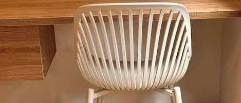 A white chair with a slatted back design, positioned in front of a wooden desk with a built-in drawer.