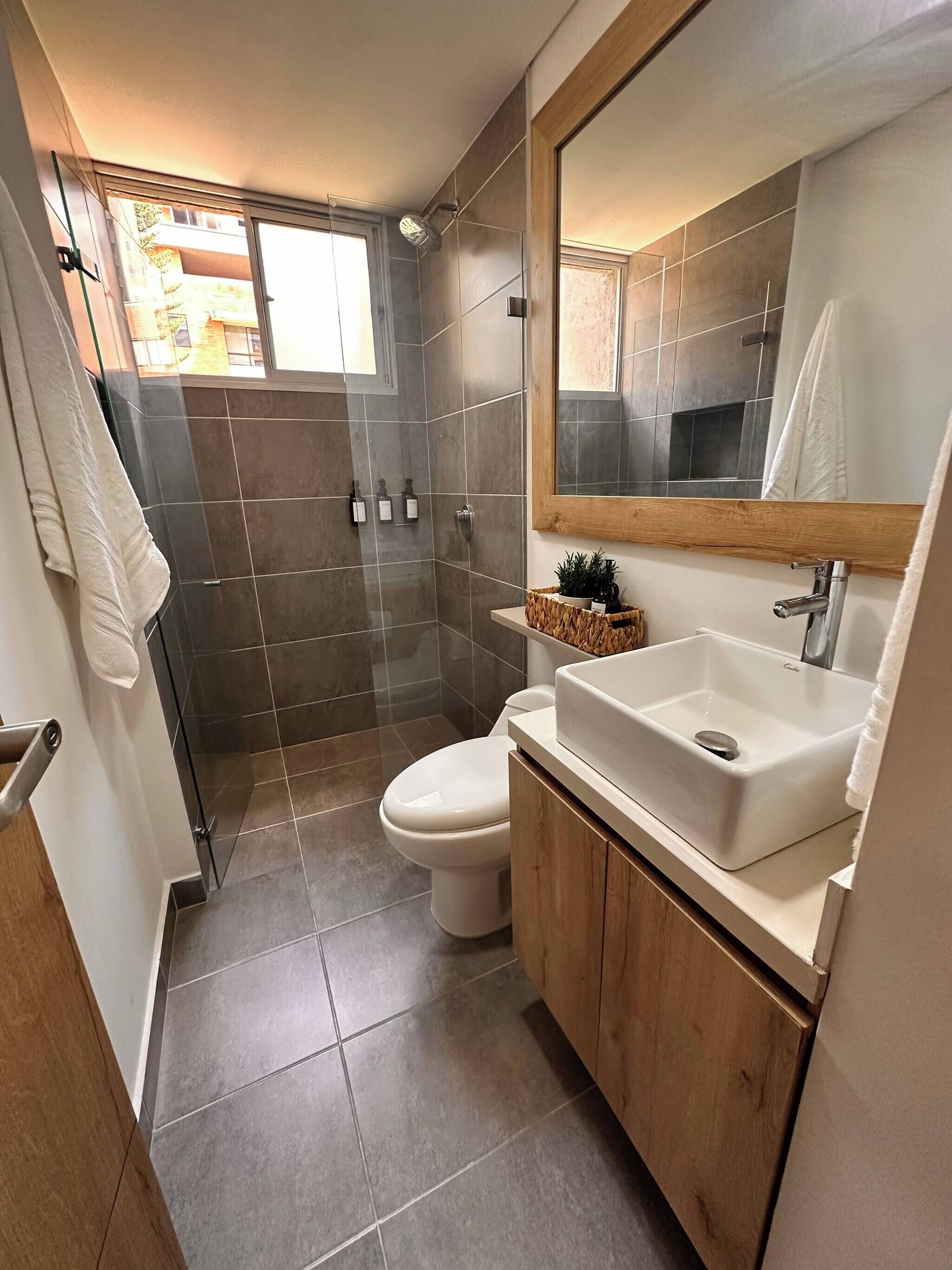 Un bagno con doccia, toilette e lavandino, con pareti in piastrelle e un mobiletto in legno.