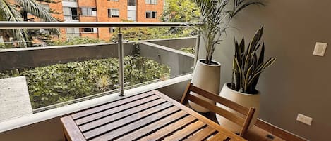 A balcony with a wooden table and chairs, potted plants, and a view of a brick building.