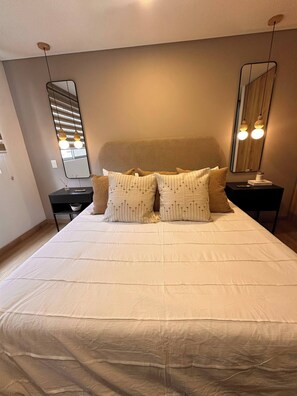 A neatly made bed with pillows, a bedside table with a lamp, and a large mirror on the wall. - Premium Village 24 7 Security Balcony Fast Wifi (Medellín)