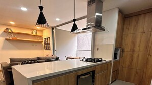A modern kitchen with a central island, wooden cabinetry, a built-in oven, and pendant lighting. - Premium Village 24 7 Security Balcony Fast Wifi (Medellín)