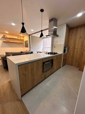 A modern kitchen with a central island, wooden cabinetry, a built-in oven, and pendant lighting. - Premium Village 24 7 Security Balcony Fast Wifi (Medellín)