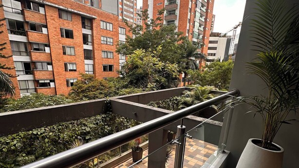 A balcony with a tiled floor, metal railing, potted plants, and a view of high-rise buildings. - Premium Village 24 7 Security Balcony Fast Wifi (Medellín)