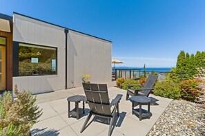 Ein modernes Gebäude mit einer Terrasse, auf der zwei Adirondack-Stühle und ein kleiner Tisch stehen.