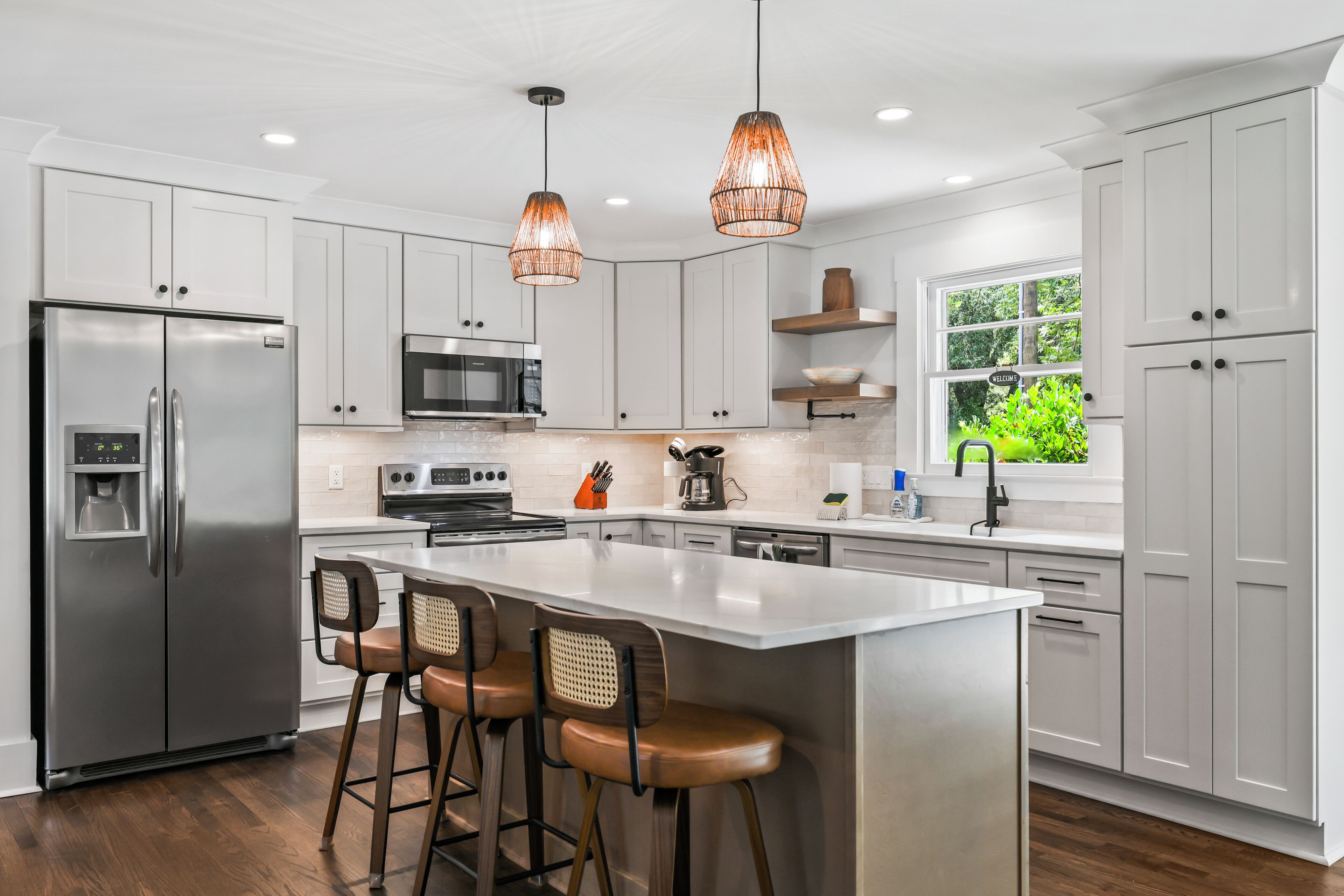 A modern kitchen with stainless steel appliances, white cabinetry, and a central island with bar stools.