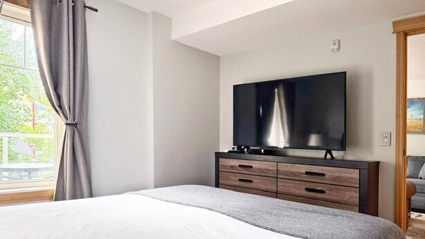 Ein Schlafzimmer mit einem Bett, einem Fernseher auf einer Holzkommode und einem Fenster mit Vorhängen.