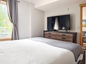 Ein Schlafzimmer mit einem Bett, einem Fernseher auf einer Holzkommode und einem Fenster mit Vorhängen.