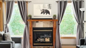 Ein Wohnzimmer mit Kamin, zwei grauen Sofas, einem Couchtisch und einem Bären-Motivbild über dem Kamin.