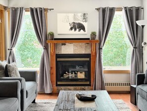 Ein Wohnzimmer mit Kamin, zwei grauen Sofas, einem Couchtisch und einem Bären-Motivbild über dem Kamin.