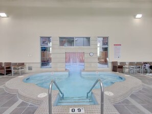 An indoor swimming pool with a tiled floor, a central diving board, and a clock on the wall. - Cozy Alpine Retreat *Waterslide~Pool~Hot Tub* (Canmore)