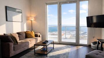 Een woonkamer met een bank, salontafel, televisie en een grote schuifglazen deur die leidt naar een balkon met uitzicht.