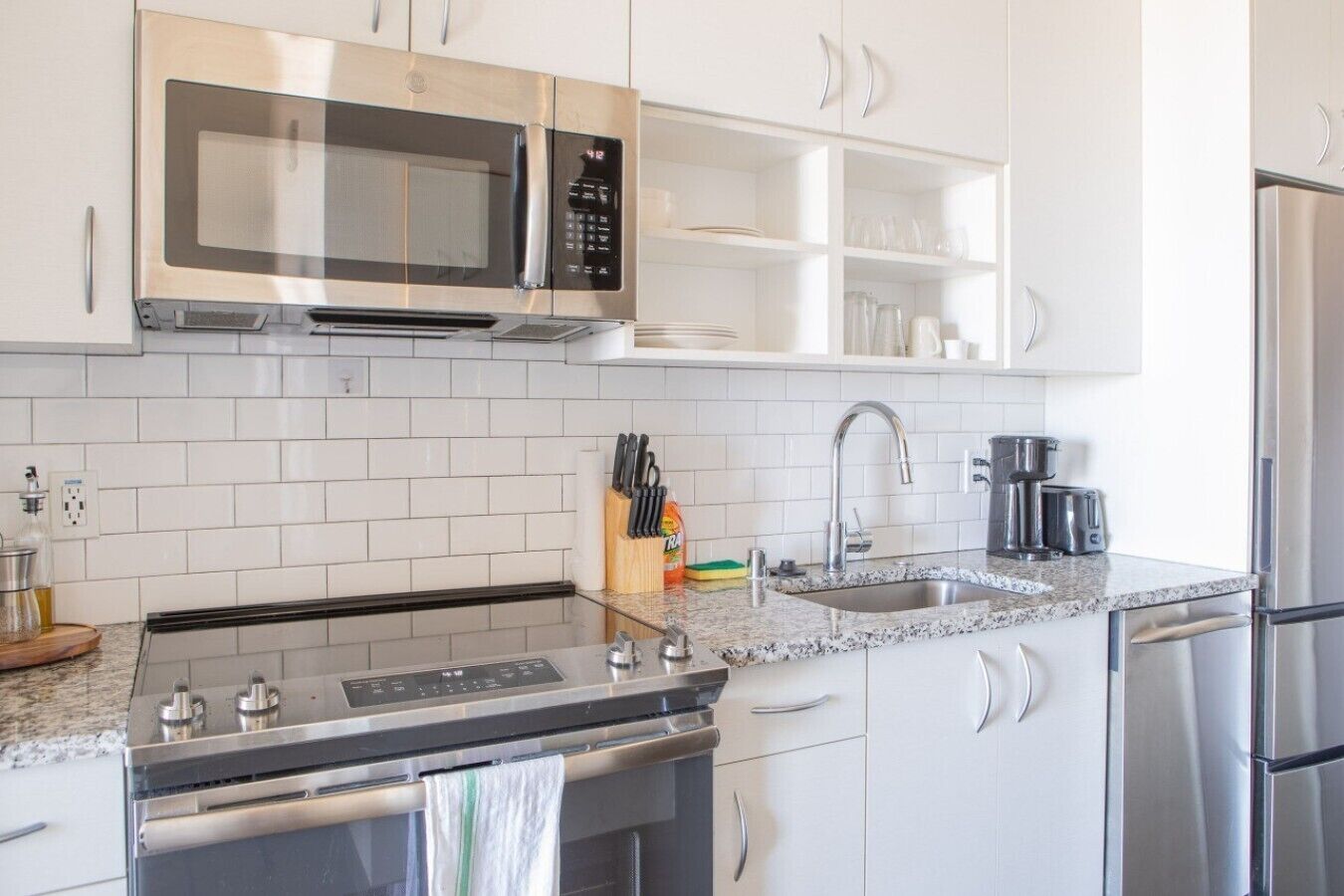 Eine moderne Küche mit Edelstahlgeräten, weißen Schränken und einer Arbeitsplatte aus Granit.