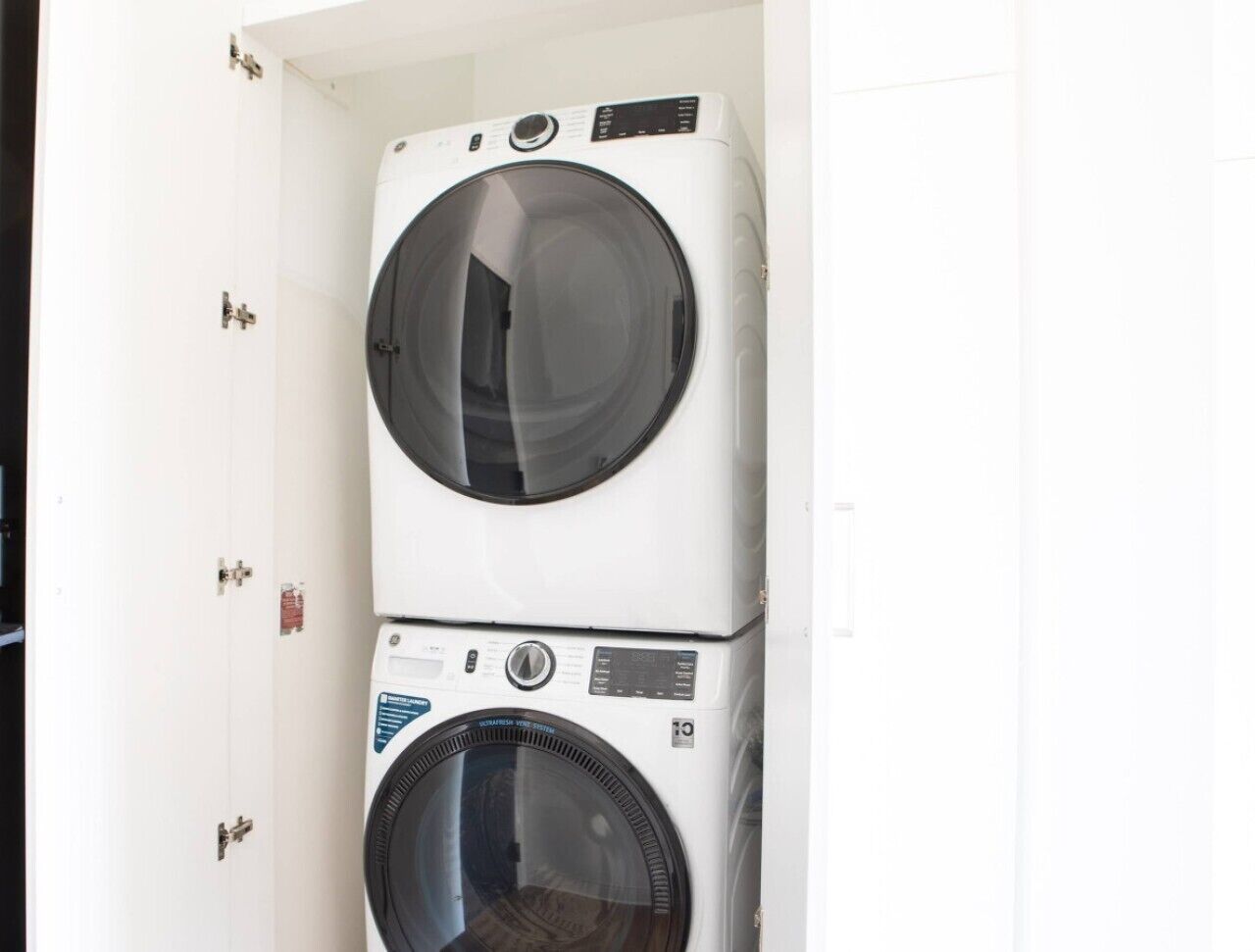 Een gestapelde wasmachine en droger in een ruimte met witte muren en een deur met een hendel.