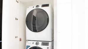 A stacked washer and dryer unit in a room with white walls and a door with a handle. - Luxury Penthouse Apt Near Brady St with Balcony and Lake View (Milwaukee)