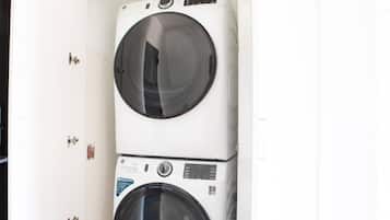 Een gestapelde wasmachine en droger in een ruimte met witte muren en een deur met een hendel.