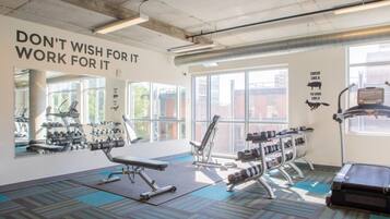 Een sportschool met trainingsapparatuur, grote ramen en motiverende tekst op de muur.