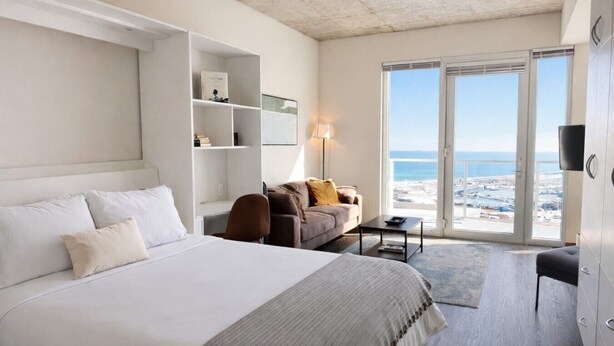 A modern hotel room with a large bed, a sofa, a desk, and a view of the beach. - Luxury Penthouse Apt Near Brady St with Balcony and Lake View (Milwaukee)